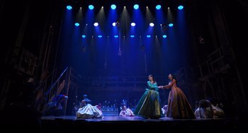 Movie still from “Hamilton” (2020), directed by Thomas Kail – Two women in dresses are shaking hands on a stage; Extreme Wide shot, Low angle