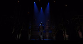 Movie still from “Hamilton” (2020), directed by Thomas Kail – A man standing on a stage in the middle of a dark room; Extreme Wide shot, Low angle