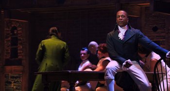 Movie still from “Hamilton” (2020), directed by Thomas Kail – A group of people sitting around a wooden table; Medium shot, Over the shoulder angle