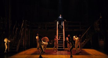 Movie still from “Hamilton” (2020), directed by Thomas Kail – A group of people standing around a man on top of stairs; Extreme Wide shot, Low angle