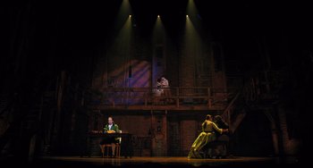 Movie still from “Hamilton” (2020), directed by Thomas Kail – A man sitting at a desk in front of an audience; Extreme Wide shot, Low angle