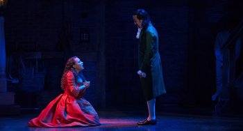 Movie still from “Hamilton” (2020), directed by Thomas Kail – A woman in a red dress and a man in a green suit; Medium shot, High angle