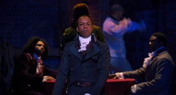 Movie still from “Hamilton” (2020), directed by Thomas Kail – A man standing in front of a group of people; Medium shot, Over the shoulder angle