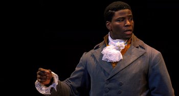 Movie still from “Hamilton” (2020), directed by Thomas Kail – A black man in a gray suit and white neck tie; Medium shot, Over the shoulder angle