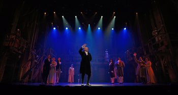 Movie still from “Hamilton” (2020), directed by Thomas Kail – A group of people standing on a stage in front of lights; Extreme Wide shot, Low angle