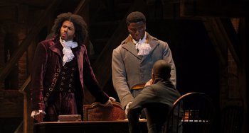 Movie still from “Hamilton” (2020), directed by Thomas Kail – A couple of men standing next to each other on top of a table; Medium shot, Over the shoulder angle