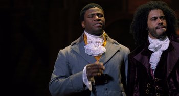 Movie still from “Hamilton” (2020), directed by Thomas Kail – A black man in a gray suit and white shirt; Medium shot, Over the shoulder angle