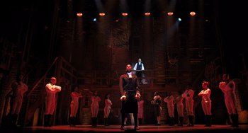 Movie still from “Hamilton” (2020), directed by Thomas Kail – A group of people standing on a stage with lights in the background; Extreme Wide shot, Low angle