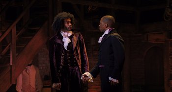 Movie still from “Hamilton” (2020), directed by Thomas Kail – Two men dressed in period clothing are holding hands; Medium shot, Over the shoulder angle