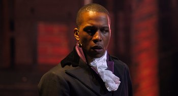 Movie still from “Hamilton” (2020), directed by Thomas Kail – A man in a black jacket and purple shirt; Close Up shot, Over the shoulder angle