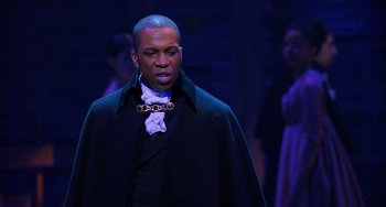 Movie still from “Hamilton” (2020), directed by Thomas Kail – A man wearing a black coat and a white shirt; Medium shot, Over the shoulder angle
