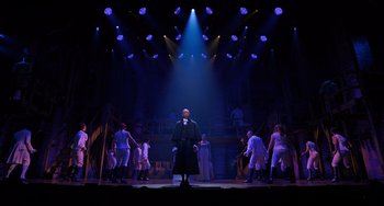 Movie still from “Hamilton” (2020), directed by Thomas Kail – A man standing in front of a group of people on a stage; Extreme Wide shot, Low angle