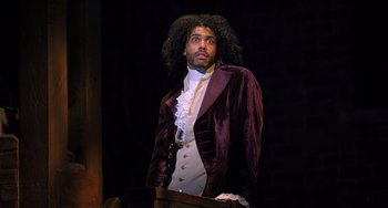 Movie still from “Hamilton” (2020), directed by Thomas Kail – A man in a purple jacket standing in front of a chair; Medium shot, Over the shoulder angle