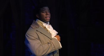 Movie still from “Hamilton” (2020), directed by Thomas Kail – A man in a brown coat and white shirt; Medium shot, High angle