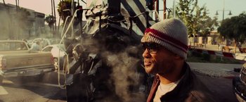 Movie still from “Hancock” (2008), directed by Peter Berg – A man wearing a hat standing next to a pile of trash; Close Up shot, Over the shoulder angle