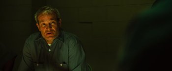 Movie still from “Hancock” (2008), directed by Peter Berg – A man sitting in a dark room looking at the camera; Close Up shot, Over the shoulder angle