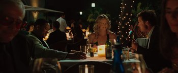 Movie still from “Hancock” (2008), directed by Peter Berg – A woman sitting at a table with a bottle of wine; Medium shot, Over the shoulder angle