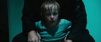 Movie still from “Hancock” (2008), directed by Peter Berg – A young boy with wet hair and blue eyes in a dark room; Close Up shot, High angle