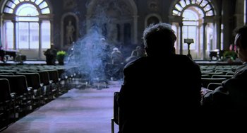 Movie still from “Hannibal” (2001), directed by Ridley Scott – An older man sitting in a chair in a room; Wide shot, Over the shoulder angle