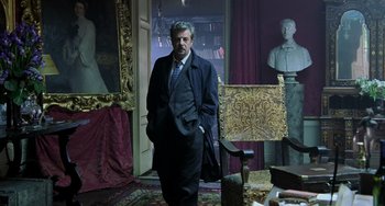 Movie still from “Hannibal” (2001), directed by Ridley Scott – A man in a suit and tie standing in front of a painting; Wide shot, Low angle