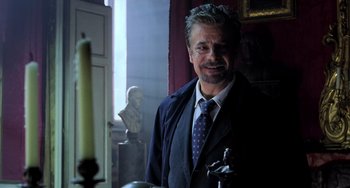 Movie still from “Hannibal” (2001), directed by Ridley Scott – A man in a suit and tie standing next to a candle; Medium shot, Over the shoulder angle