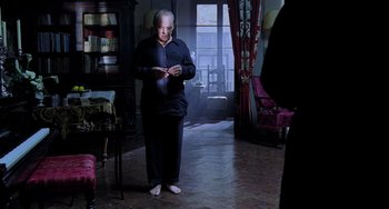 Movie still from “Hannibal” (2001), directed by Ridley Scott – An older man standing in a living room with his feet on the ground; Wide shot, High angle
