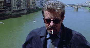 Movie still from “Hannibal” (2001), directed by Ridley Scott – A person wearing a suit and sunglasses smoking a cigarette; Close Up shot, Low angle