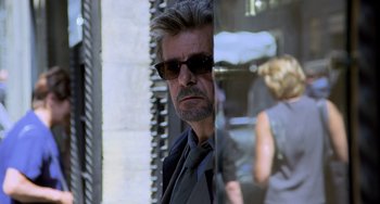 Movie still from “Hannibal” (2001), directed by Ridley Scott – A man wearing sunglasses and a suit and tie; Close Up shot, Over the shoulder angle