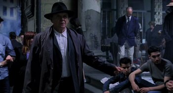 Movie still from “Hannibal” (2001), directed by Ridley Scott – An old man in a hat and a coat is standing in front of other men; Medium shot, Over the shoulder angle