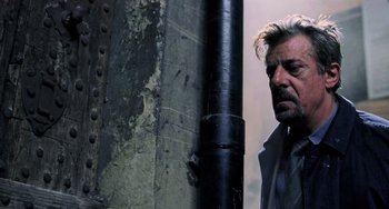 Movie still from “Hannibal” (2001), directed by Ridley Scott – A man standing next to a metal pole in an alley; Close Up shot, Low angle