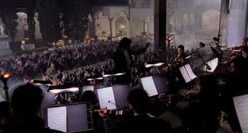 Movie still from “Hannibal” (2001), directed by Ridley Scott – A large crowd of people are gathered in the dark to watch a concert; Extreme Wide shot, High angle