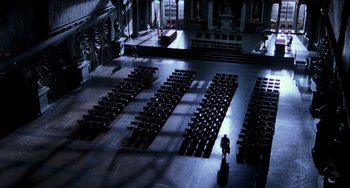 Movie still from “Hannibal” (2001), directed by Ridley Scott – A man standing in a large room with rows of chairs; Extreme Wide shot, High angle