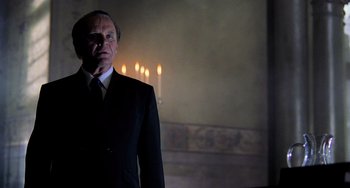 Movie still from “Hannibal” (2001), directed by Ridley Scott – A man in a suit and tie standing in front of candles; Medium shot, Low angle