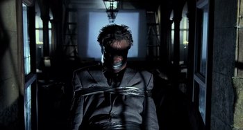 Movie still from “Hannibal” (2001), directed by Ridley Scott – A man tied to a chair in a dark room; Medium shot, Low angle