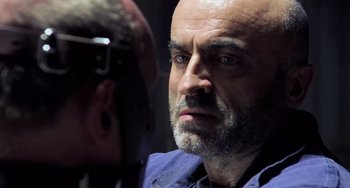 Movie still from “Hannibal” (2001), directed by Ridley Scott – A man with a bald head is looking at another man; Close Up shot, Over the shoulder angle