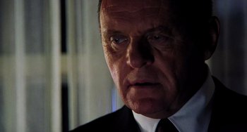 Movie still from “Hannibal” (2001), directed by Ridley Scott – An older man wearing a suit and tie looking at the camera; Close Up shot, Low angle