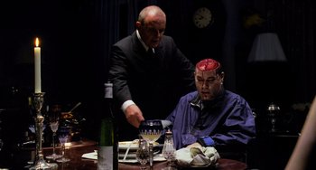 Movie still from “Hannibal” (2001), directed by Ridley Scott – A man sitting at a dinner table with another man standing next to him; Medium shot, Over the shoulder angle