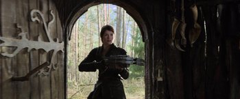 Movie still from “Hansel & Gretel: Witch Hunters” (2013), directed by Tommy Wirkola – A woman holding a gun while standing in front of trees; Medium shot, Low angle