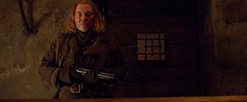 Movie still from “Hansel & Gretel: Witch Hunters” (2013), directed by Tommy Wirkola – A man holding a gun while standing next to a wooden wall; Medium shot, Low angle