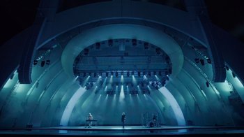 Movie still from “Happier Than Ever: A Love Letter to Los Angeles” (2021), directed by Patrick Osborne – A stage lit up with lights and a man standing on a stage; Extreme Wide shot, High angle