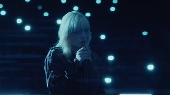 Movie still from “Happier Than Ever: A Love Letter to Los Angeles” (2021), directed by Patrick Osborne – A woman with blond hair is holding a microphone in her hand; Medium shot, High angle