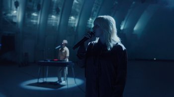 Movie still from “Happier Than Ever: A Love Letter to Los Angeles” (2021), directed by Patrick Osborne – A woman singing into a microphone in front of a man; Wide shot, Over the shoulder angle