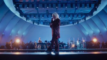 Movie still from “Happier Than Ever: A Love Letter to Los Angeles” (2021), directed by Patrick Osborne – A woman standing on a stage holding a microphone; Wide shot, Low angle