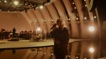 Movie still from “Happier Than Ever: A Love Letter to Los Angeles” (2021), directed by Patrick Osborne – A woman holding a microphone in front of an audience; Wide shot, High angle
