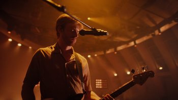 Movie still from “Happier Than Ever: A Love Letter to Los Angeles” (2021), directed by Patrick Osborne – A man holding a guitar in front of a microphone on a stage; Medium shot, Low angle