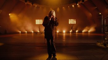 Movie still from “Happier Than Ever: A Love Letter to Los Angeles” (2021), directed by Patrick Osborne – A person standing on a stage with a microphone; Wide shot, High angle