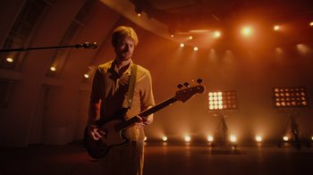 Movie still from “Happier Than Ever: A Love Letter to Los Angeles” (2021), directed by Patrick Osborne – A man holding a guitar in front of a stage; Wide shot, Low angle