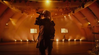 Movie still from “Happier Than Ever: A Love Letter to Los Angeles” (2021), directed by Patrick Osborne – A woman singing into a microphone on a stage; Wide shot, Low angle