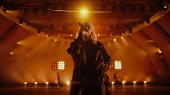 Movie still from “Happier Than Ever: A Love Letter to Los Angeles” (2021), directed by Patrick Osborne – A woman in black jacket holding a microphone; Wide shot, Low angle