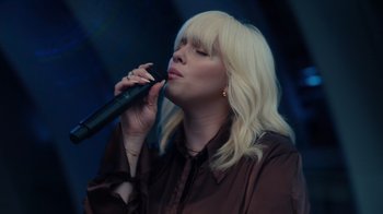 Movie still from “Happier Than Ever: A Love Letter to Los Angeles” (2021), directed by Patrick Osborne – A woman with blonde hair is singing into a microphone; Close Up shot, Low angle